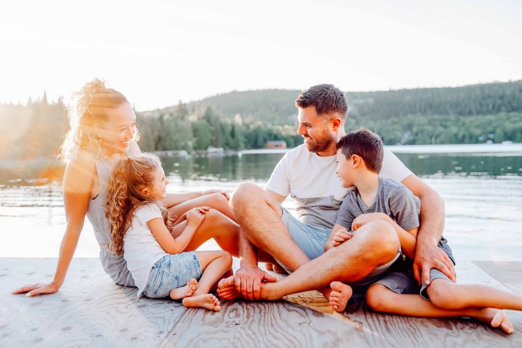 Familie sitz bei Sonnenuntergang am Seeufer auf einem Steg