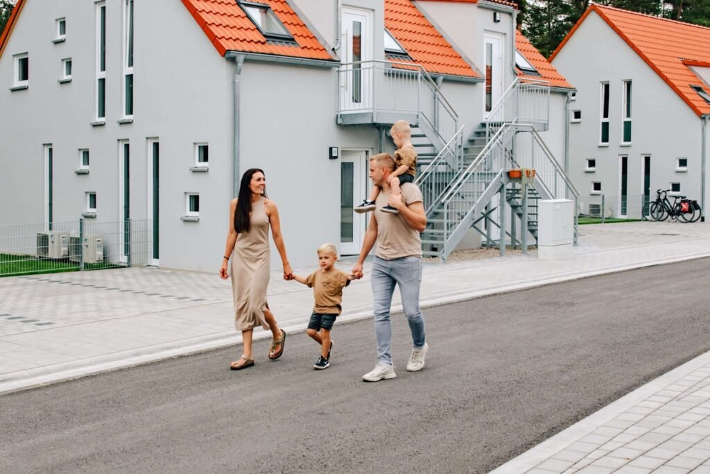 Eine Familie mit 2 Kindern spaziert über eine Straße, im Hintergrund sind Ferienhäuser mit zwei Fahrrädern davor