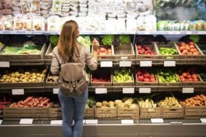 Eine Frau steht vor einem Gemüseregal im Supermarkt