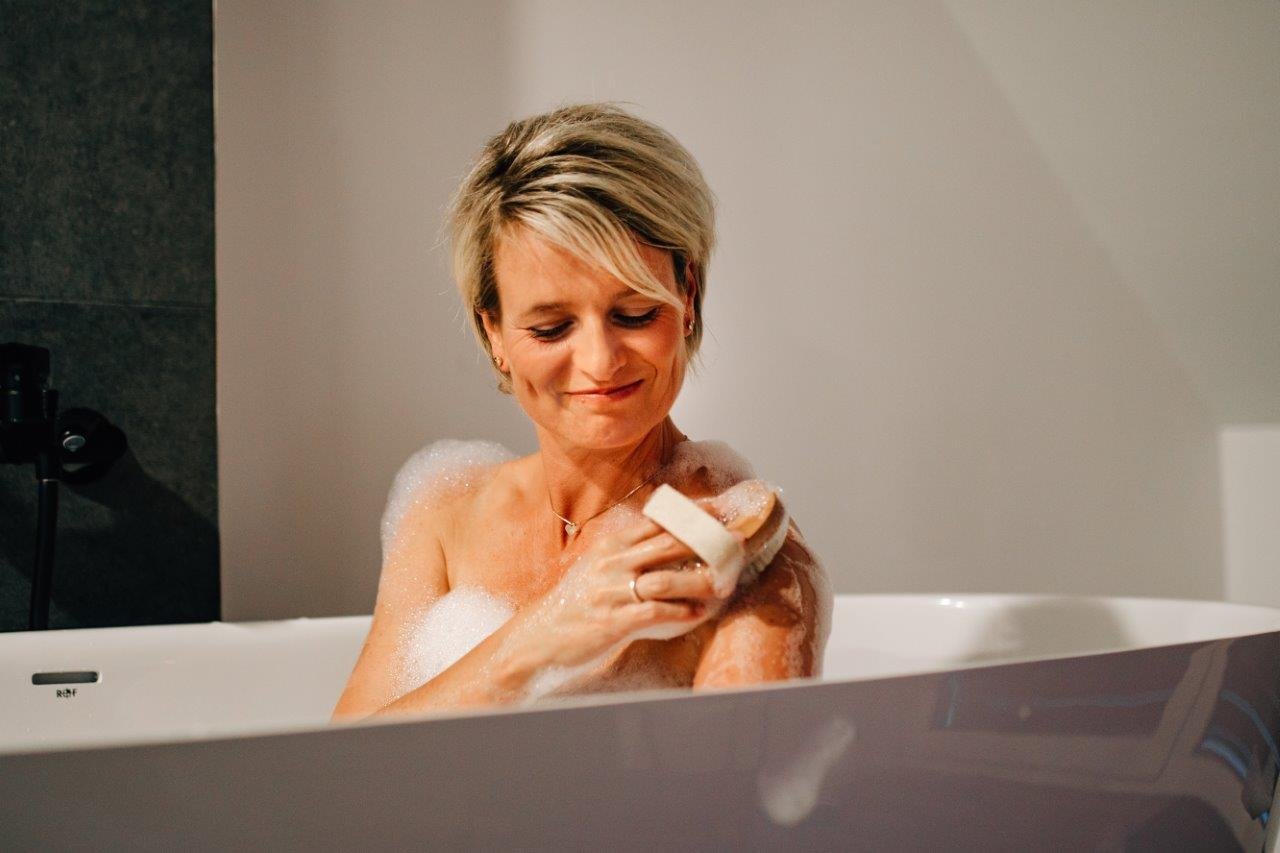 Dame sitzt in einer Badewanne und nutzt einen Peeling Handschuh